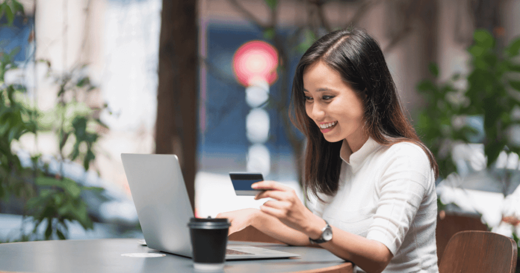 Woman sitting at her laptop with her credit card out happily making a purchase online. 