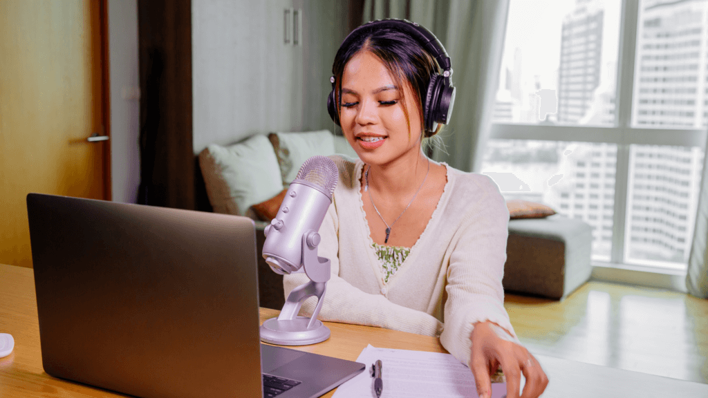 Woman sitting at a desk with her laptop and a microphone recording a podcast.