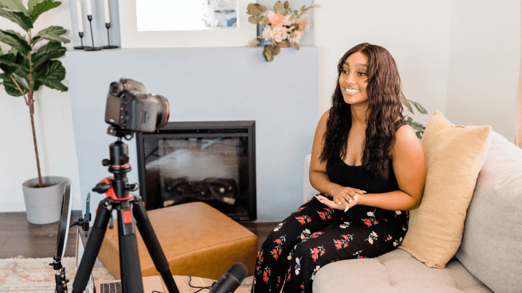 Woman sitting on a couch in front of a fireplace recording with a DSLR camera for YouTube.