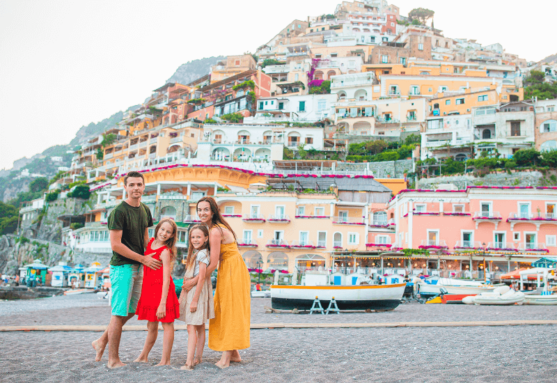 A family of four traveling on vacation and posing for a picture in front of colorful homes. 