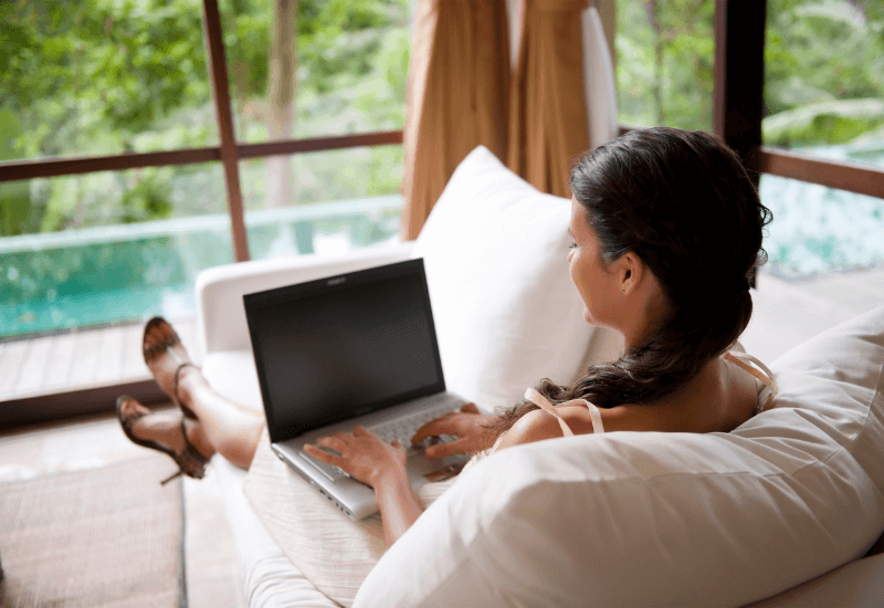 A Mompreneur working at home on her laptop while sitting on a comfortable couch with a great view of her backyard pool.