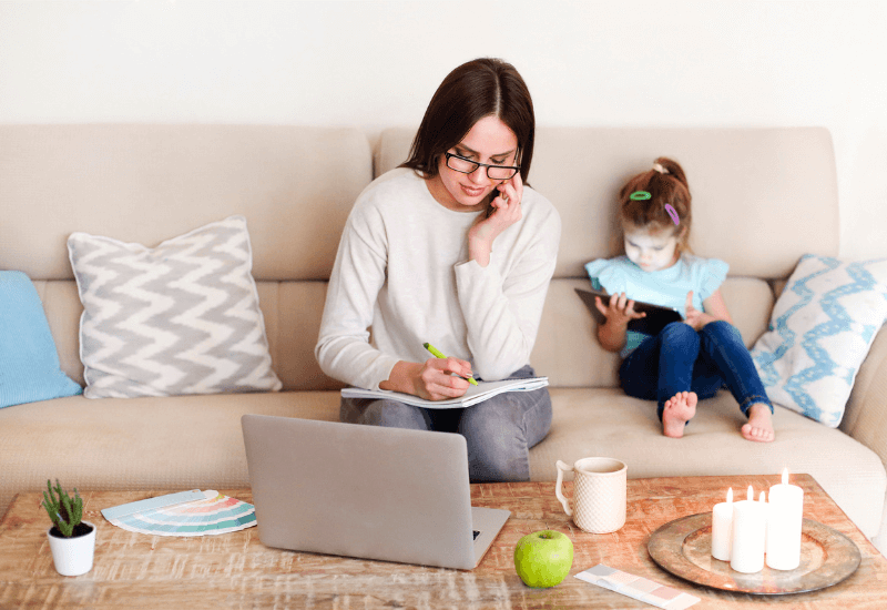 A Mompreneur sitting on the couch with daughter while working.