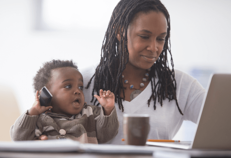 mompreneur holding her baby while working on her laptop