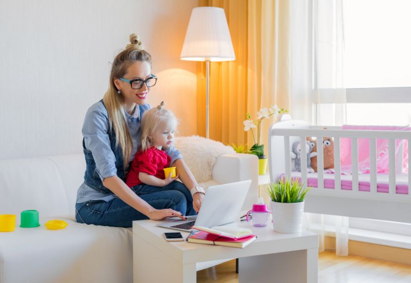 Mompreneur working at home on her laptop with her toddler on her lap.