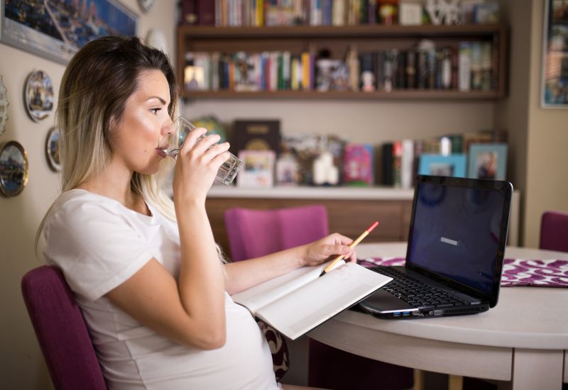 Pregnant mom working from home on her laptop while drinking some water.